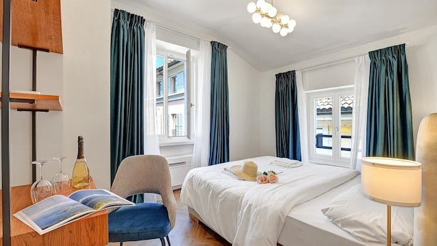 A hotel room with a bed, a desk with a chair, a lamp, and a window with curtains. - Novos Diamond in Lugano (Lugano)