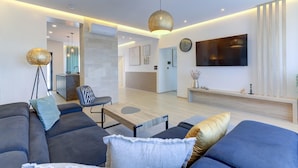 A modern living room with a sofa, coffee table, and pendant lights. There is a television mounted on the wall and a small table with decorative items. - Villa One in Novi Vinodolski (Novi Vinodolski)