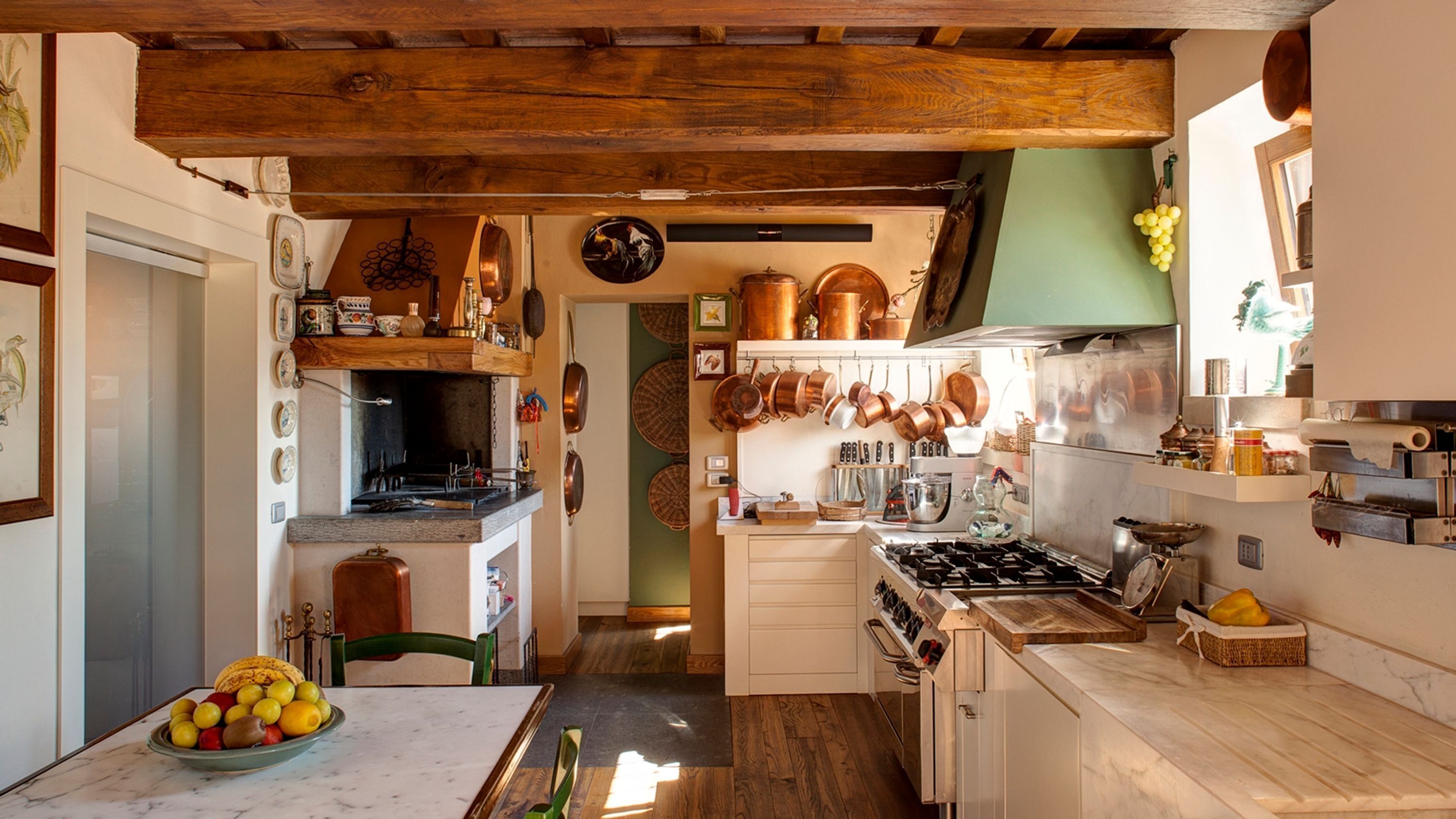 A kitchen with wooden beams, copper cookware, and a fruit bowl on the counter.