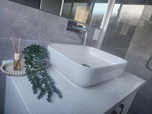Un bagno moderno con un lavabo a incasso bianco, box doccia in vetro e una piccola pianta sul piano di lavoro.