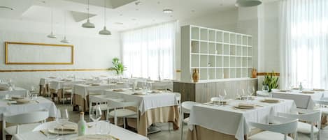 A restaurant with multiple tables set for dining, white walls, and a modern ceiling design.
