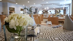 Un comedor con mesas dispuestas para el servicio, un jarrón con flores blancas y un mantel con estampado.