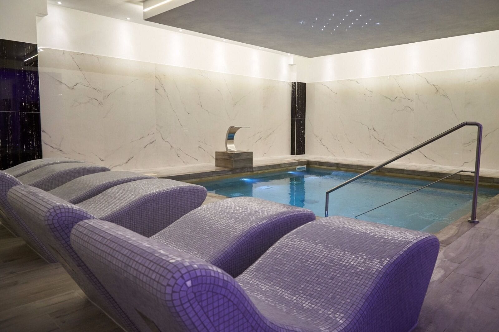Una piscina interior moderna con una pared de mármol y una escalera.
