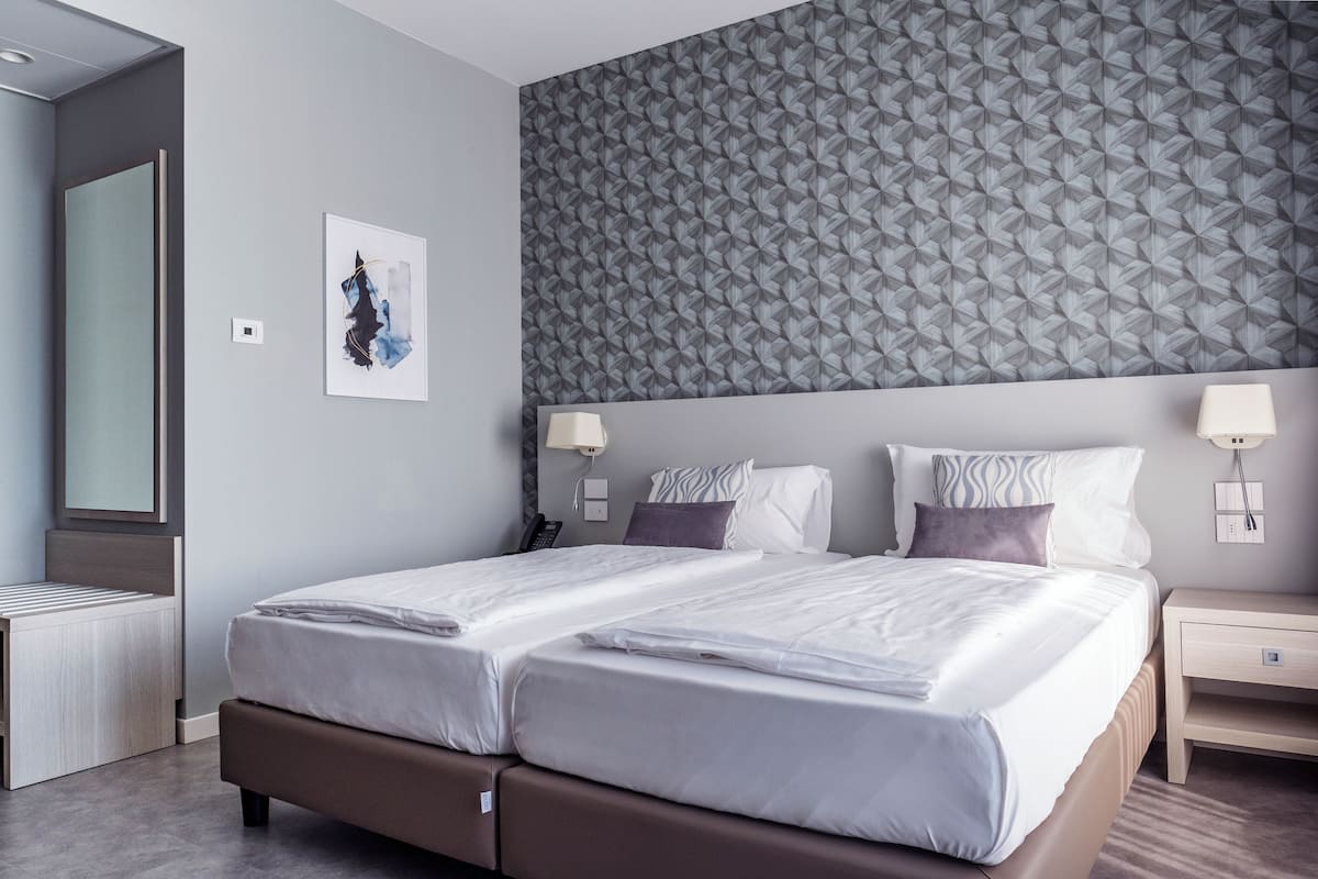 A double bed with a headboard, bedside tables, a mirror, and a wall with a geometric pattern.