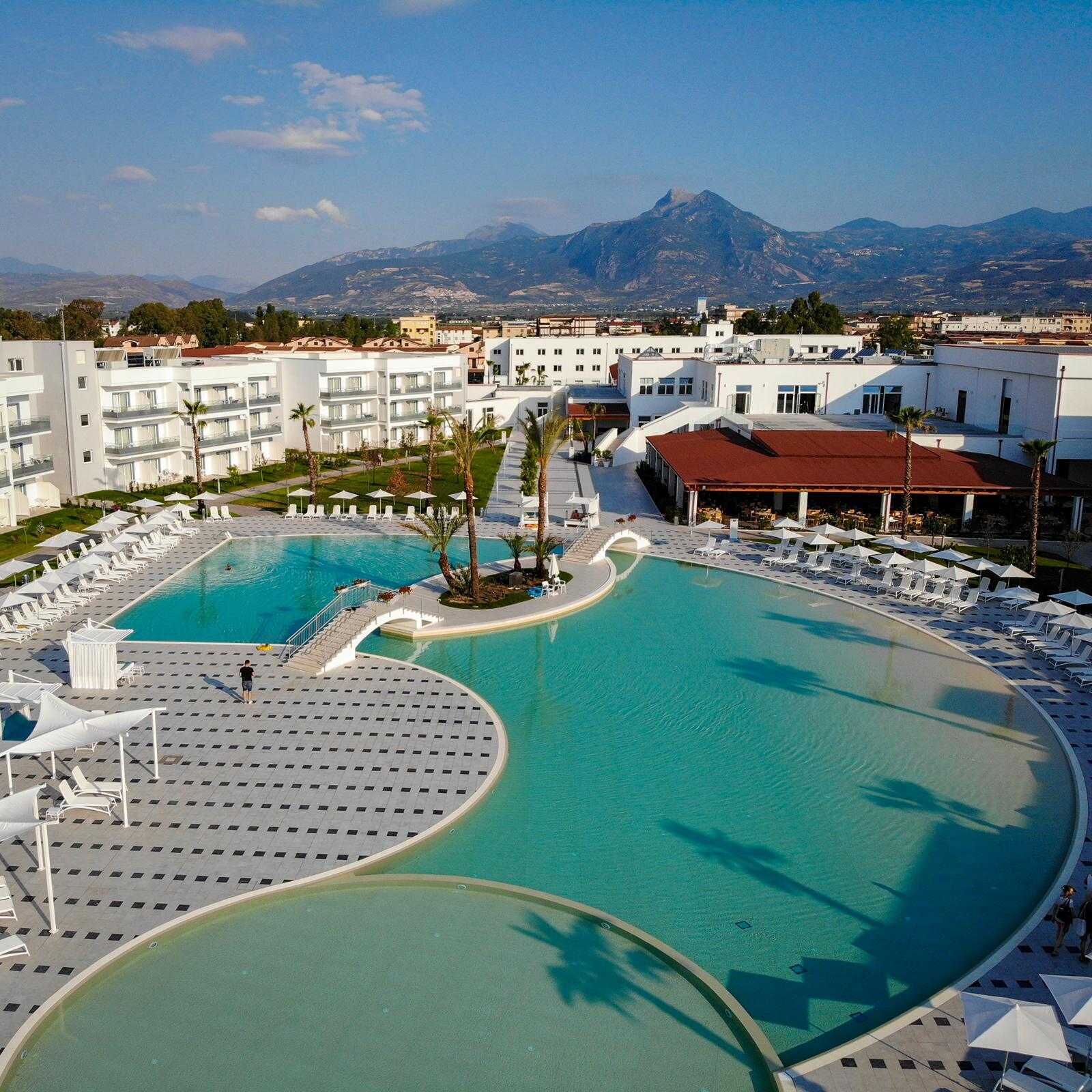 A resort with a large pool, multiple lounge areas, and a view of mountains in the background.