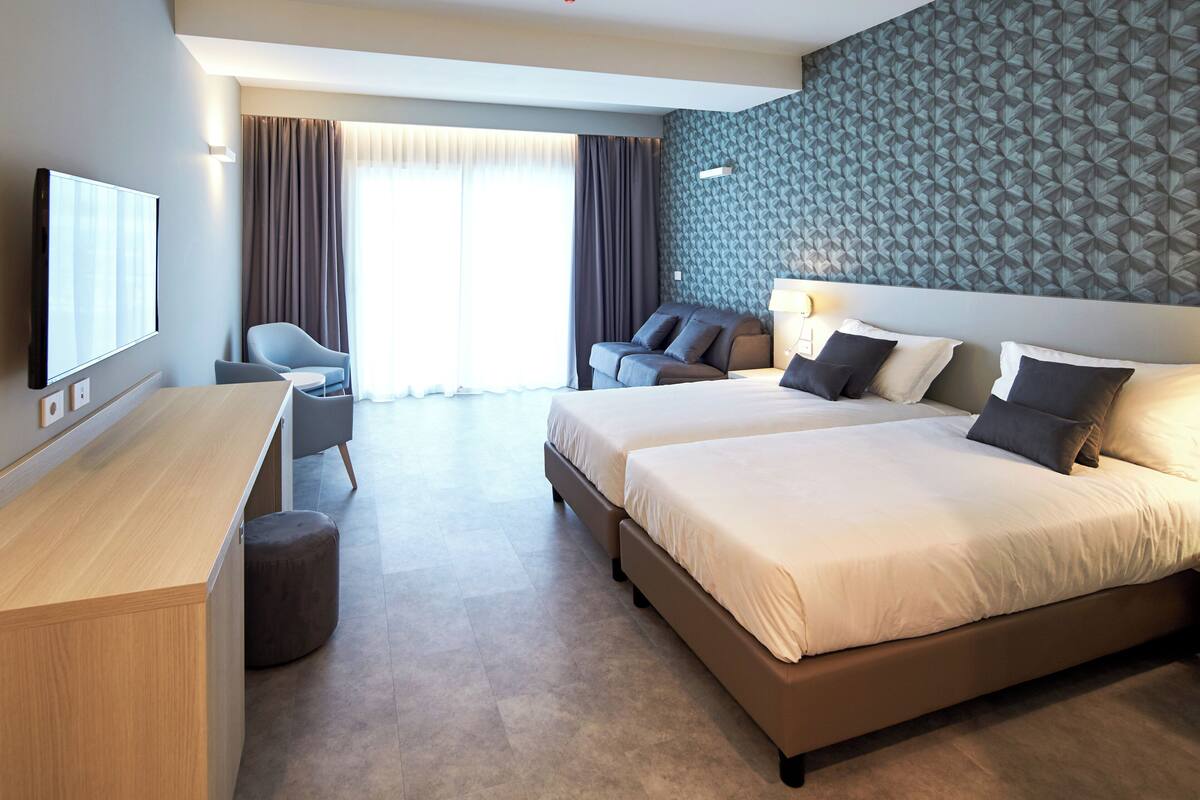A hotel room with a large bed, a desk, a chair, and a TV.
