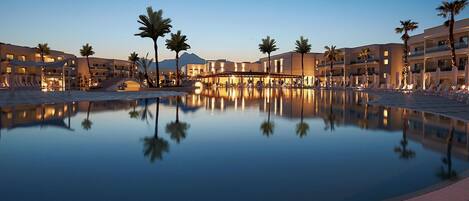 Un área de piscina tranquila con palmeras y edificios modernos reflejándose en el agua.