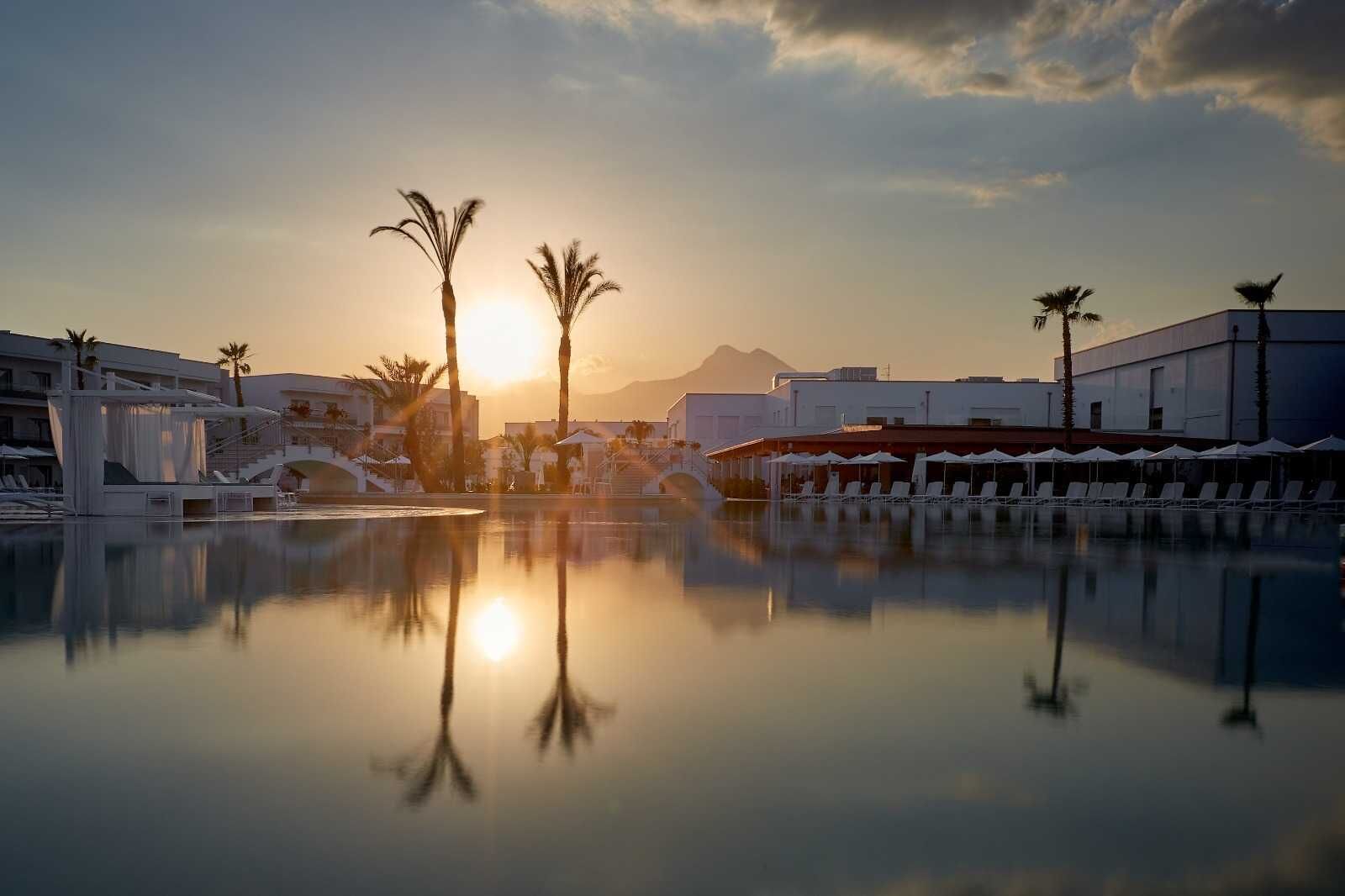 Piscina de resort con palmeras y una montaña al fondo.