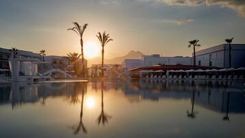 A resort pool with palm trees and a mountain in the background.