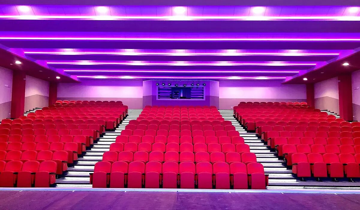 A theater with red seats, a stage, and purple lighting.