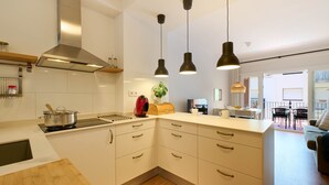 Una cocina moderna con armarios blancos, extractor de acero inoxidable e iluminación colgante.