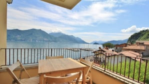 Ein Balkon mit Holztisch und Stühlen mit Blick auf einen See, im Hintergrund Berge.