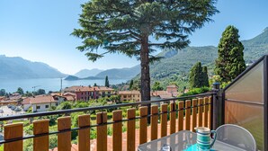 A balcony with a table, a pitcher, and glasses, overlooking a lake and buildings. - CO RI Appartamenti 3 (Menaggio)