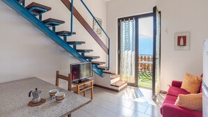 A modern living room with a staircase, a dining area, a sofa, and a view through a glass door. - CO RI Appartamenti 3 (Menaggio)