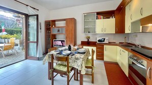Une cuisine moderne avec des meubles en bois, une table à manger pour quatre personnes et une porte-fenêtre coulissante donnant sur une terrasse extérieure.