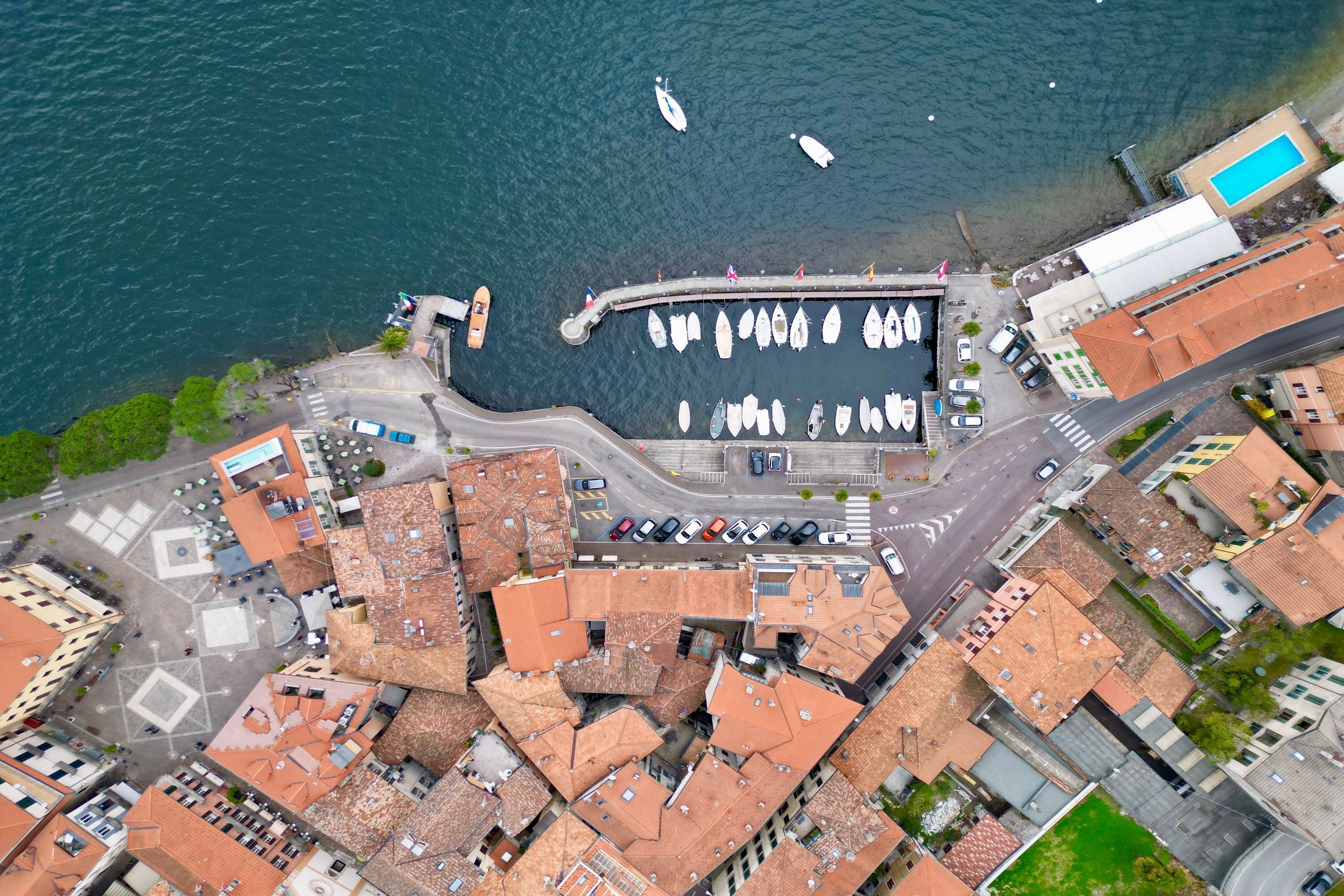 An aerial view of a coastal town with a marina, boats, and buildings with red-tiled roofs.