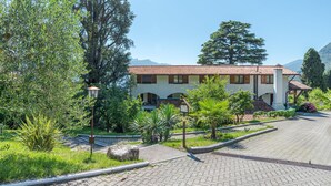 A building with a tiled roof, surrounded by lush greenery and a paved driveway. - CO RI Appartamenti 1 (Menaggio)