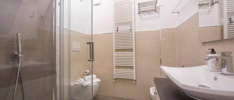 A modern bathroom with a glass-enclosed shower, a white toilet, and a beige tiled floor.