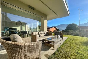 A patio area with wicker furniture, a glass door leading to a dining area, and a view of mountains. - Modern House Apartment 1 (Menaggio)