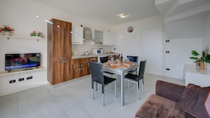 Una cucina moderna con mobili bianchi, una porta in legno e un'area da pranzo con tavolo apparecchiato per quattro persone.