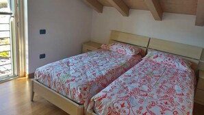 Una camera da letto con soffitto in legno, un letto con lenzuola fantasia, un comodino e una finestra con tende.