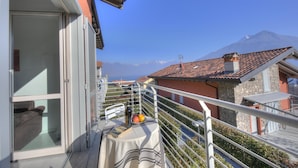 Un balcone con un tavolo apparecchiato per due, vista su una montagna e edifici circostanti.