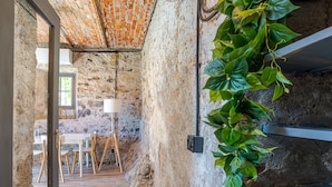 A rustic room with exposed stone walls, a wooden floor, a dining table with chairs, and a hanging plant. - Casa di Pietra Menaggio (Menaggio)