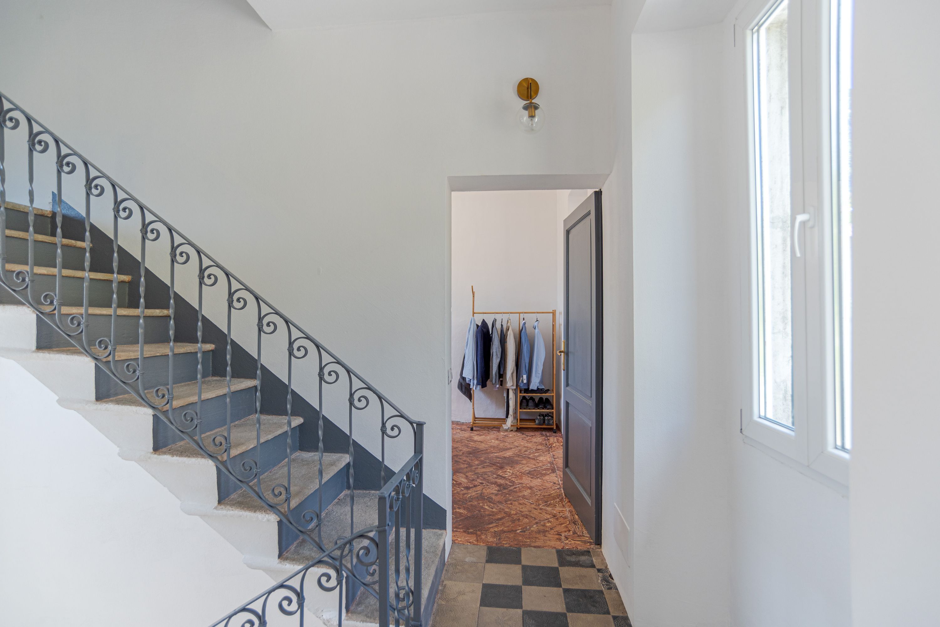 A staircase with a metal railing leading to a room with a shoe rack and clothes hanging.