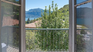 A balcony with a view of a lake, mountains, and a building with a red roof. - Casa di Pietra Menaggio (Menaggio)