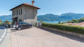 A stone building with a red-tiled roof, a paved driveway, and a view of mountains and a lake. - Casa di Pietra Menaggio (Menaggio)