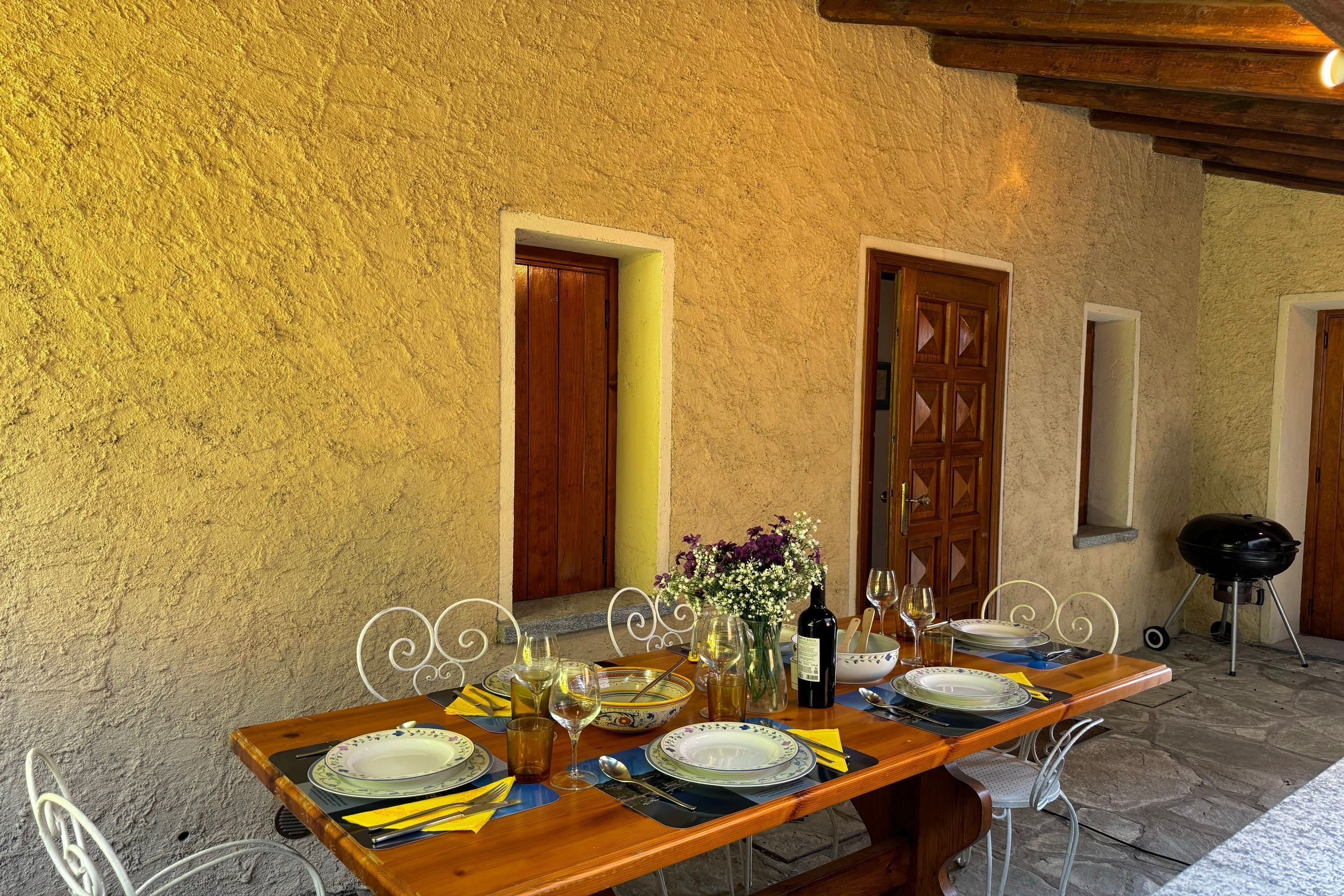 Un'area pranzo all'aperto con un tavolo di legno apparecchiato per due, circondata da muri e porte in pietra.