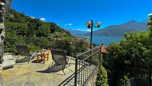 A terrace with two lounge chairs, a small table with a glass of water, and a view of a lake and mountains. - Villetta Alessia in Menaggio (San Siro)