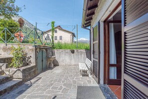 A stone-paved courtyard with a bench, a metal gate, and a building with a closed shutter. - Casa Achille Pianello (Pianello del Lario)