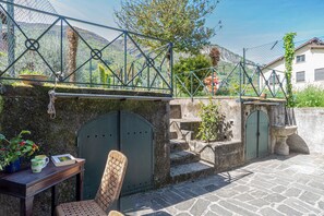 A stone patio with a metal fence, a chair, a table with a book and a mug, and a view of mountains. - Casa Achille Pianello (Pianello del Lario)