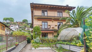 A multi-story building with balconies, a garden area with plants and a greenhouse, and a stone pathway leading to the entrance. - CO RI Appartamenti Dependance (Menaggio)