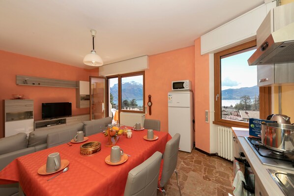 A dining area with a table set for four, a kitchen with modern appliances, and a view of mountains through large windows.