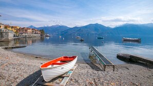 A boat docked on a pebbled shore with a mountain backdrop and calm water. - Menaggio Tosca 2 in Menaggio (Menaggio)