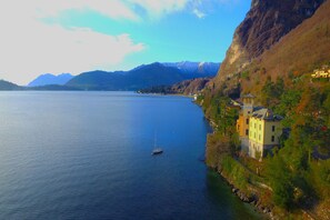 A lakeside view with a small sailboat, a building with a yellow facade, and mountains in the background. - Villa Evelyn Terrazzo (Menaggio)
