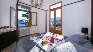 Ein Schlafzimmer mit einem großen Bett, einem Schminktisch, einem Nachttisch, einer Lampe und Meerblick durch große Fenster.