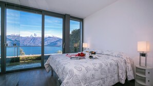 A bedroom with a large bed, two bedside lamps, and a view of mountains through floor-to-ceiling windows. - Sant Andrea Giardino (Menaggio)