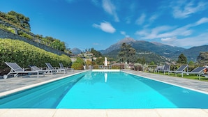 En swimmingpool med solstolar, en stenlagd gång och en bergig bakgrund.