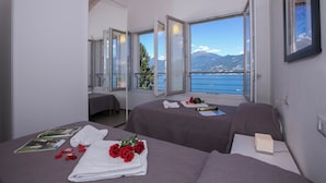 A hotel room with two beds, a balcony with a view of the sea and mountains, and a large window. - Paradiso di Menaggio Penthouse (Menaggio)