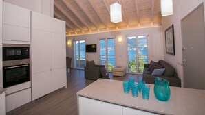 A modern kitchen with built-in appliances, a dining area with a white table, and a living room with a sofa and a TV. - Paradiso di Menaggio Penthouse (Menaggio)