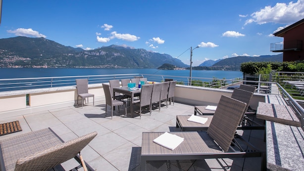 A terrace with wicker furniture, a table with chairs, and a view of the lake and mountains. - Paradiso di Menaggio Penthouse (Menaggio)