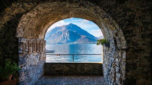 An arched stone doorway leading to a cobblestone courtyard with a view of a mountain and lake. - La Piazza Menaggio in Menaggio (Menaggio)