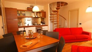 A modern kitchen with wooden cabinets, a dining table set for four, and a red sofa in the living area. - La Piazza Menaggio in Menaggio (Menaggio)