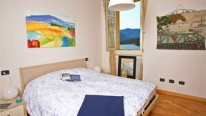 A bedroom with a bed, a nightstand, a lamp, and two paintings on the wall. - La Piazza Menaggio in Menaggio (Menaggio)