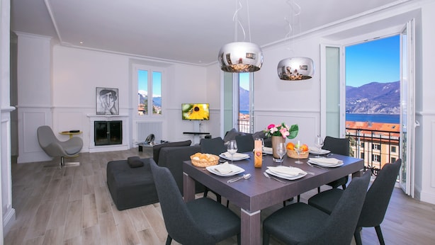 A modern dining area with a large table set for six, surrounded by dark chairs. A fireplace with a TV mounted above it is visible in the background. - Menaggio Royale in Menaggio (Menaggio)