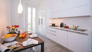 A modern kitchen with white cabinets, a gas stove, and a sink. There is a dining table with a bowl of fruit and a magazine. - Menaggio Royale in Menaggio (Menaggio)