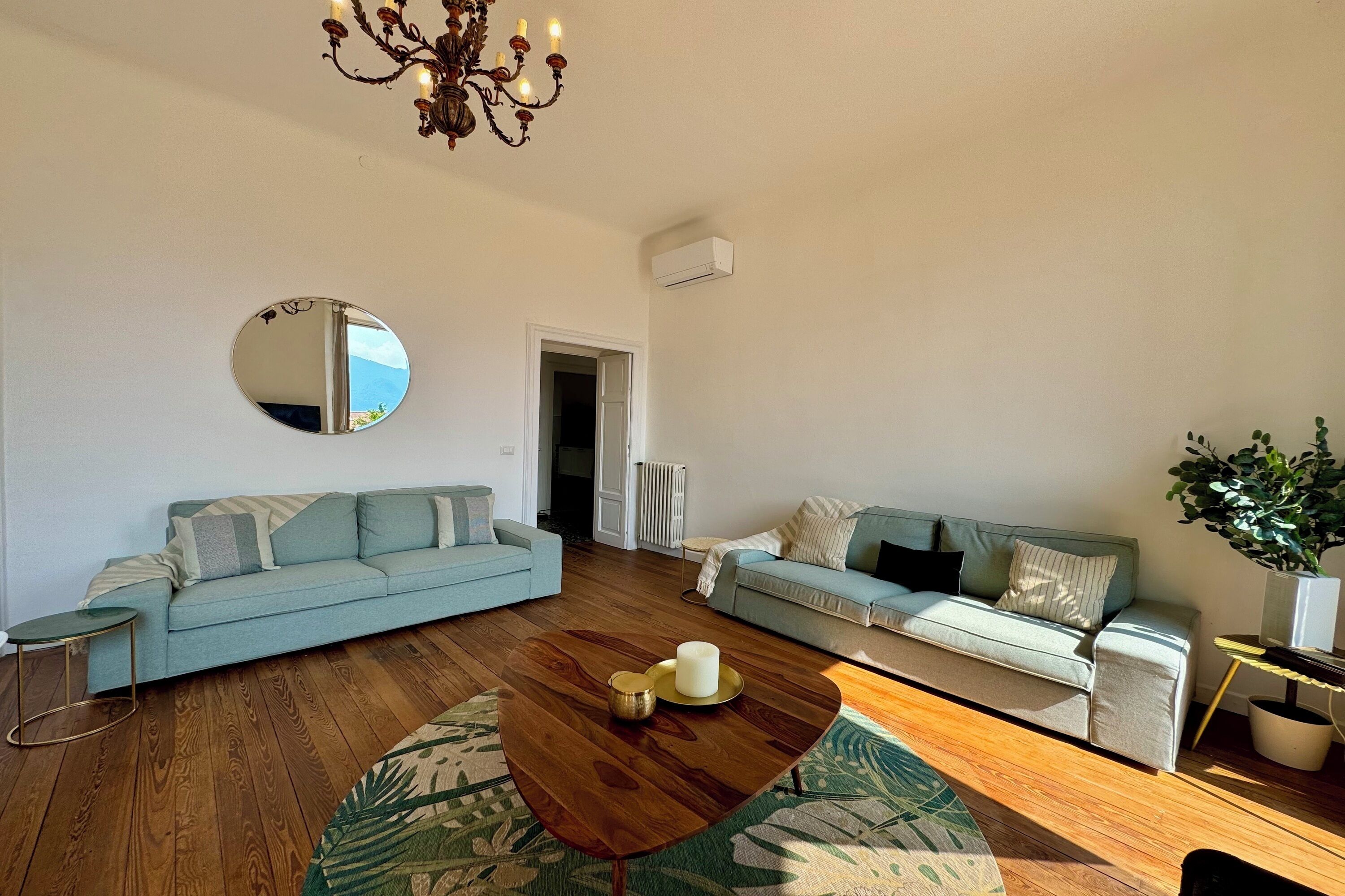 A modern living room with two light blue sofas, a wooden coffee table, a round mirror, and a chandelier.